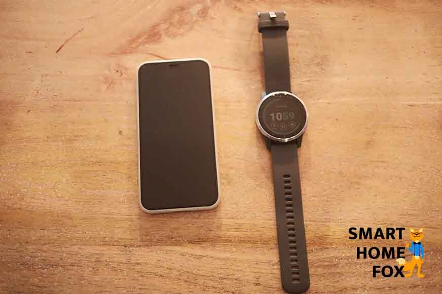 Garmin vivoactive 4 рядом с мобильным телефоном на столе. 